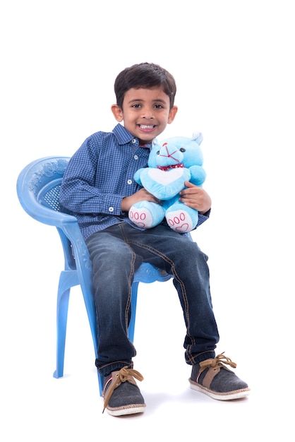 Kleiner Junge, der mit seinem ausgestopften Teddybär auf weißem Hintergrund spielt