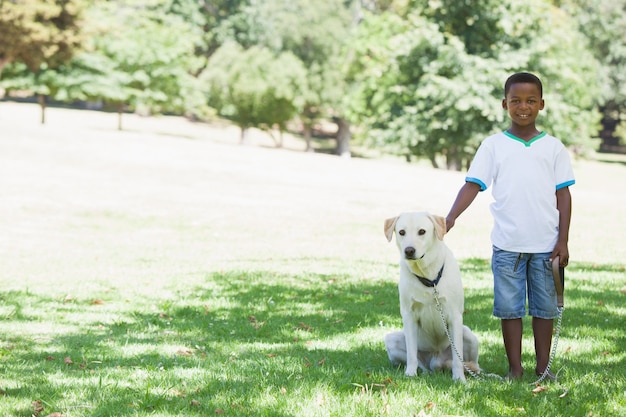 Kleiner Junge, der mit seinem Haustier Labrador im Park steht