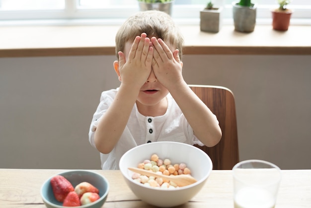 Kleiner Junge, der seine Augen beim Frühstücken bedeckt