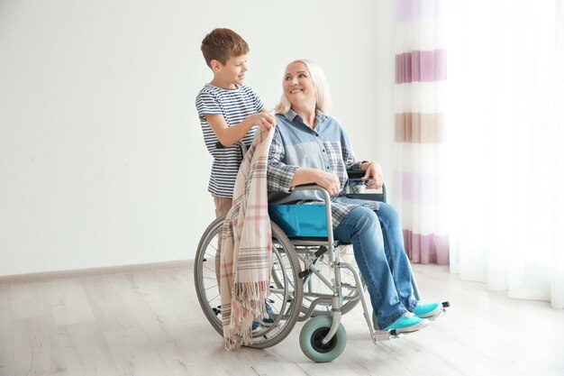 Kleiner Junge, der sich drinnen um reife Frau im Rollstuhl kümmert