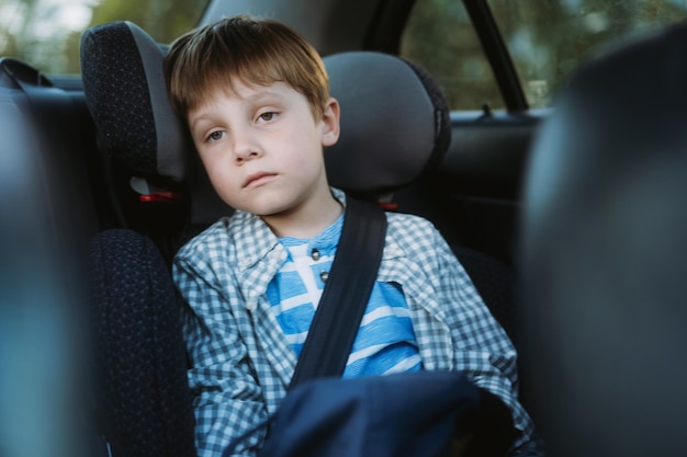 Kleiner Junge, der sich krank fühlt, wenn er mit dem Auto fährt und im Kindersitz sitzt, der mit einem Gurt befestigt ist