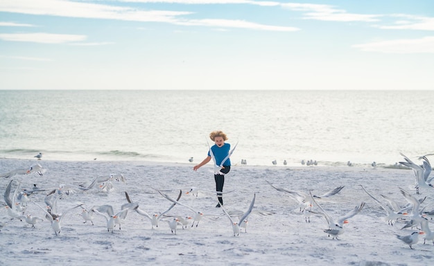 Kleiner Junge, der Spaß am Miami Beach hat, glückliches süßes Kind, das in der Nähe des Ozeans läuft und Möwenvögel jagt