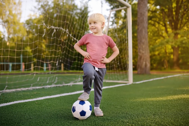 Kleiner Junge, der Spaß hat, ein Fußball- / Fußballspiel am Sommertag zu spielen. Aktiv im Freien Spiel / Sport für Kinder.