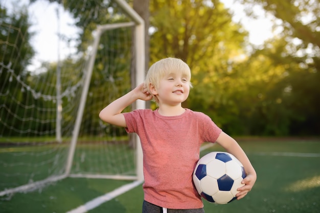 Kleiner Junge, der Spaß hat, ein Fußball- / Fußballspiel am Sommertag zu spielen.