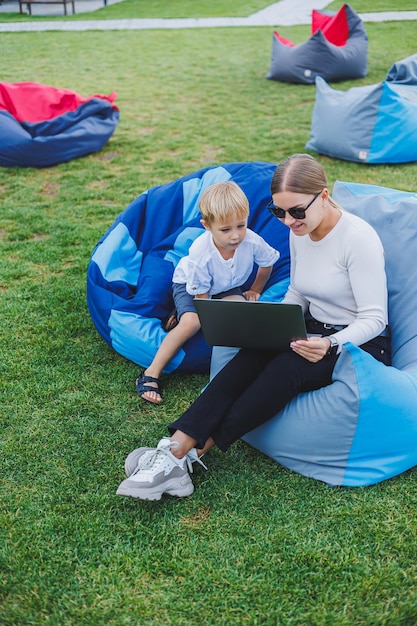 Kleiner Junge, der Spaß hat, im Sommer oder Frühling im Park im Freien auf Sack zu sitzen Familienurlaub von Mutter und Sohn an der frischen Luft