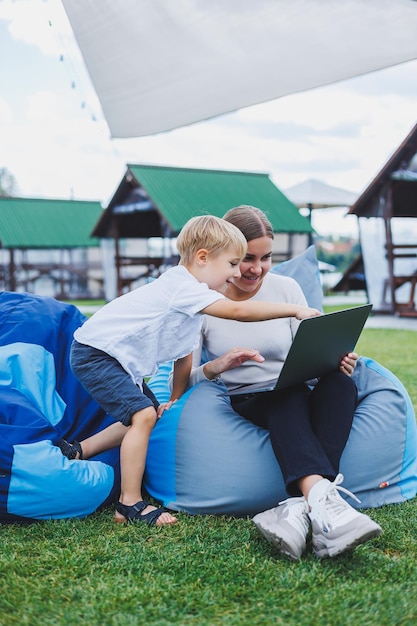 Kleiner Junge, der Spaß hat, im Sommer oder Frühling im Park im Freien auf Sack zu sitzen Familienurlaub von Mutter und Sohn an der frischen Luft