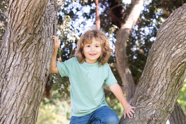 Kleiner Junge, der versucht, auf einen Baum zu klettern, Kinder, die auf einen Baum klettern. Glücklicher Junge, der den Sommertag in einem Gard genießt