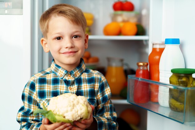 Kleiner Junge, der vor offenem Kühlschrank steht und Essen wählt