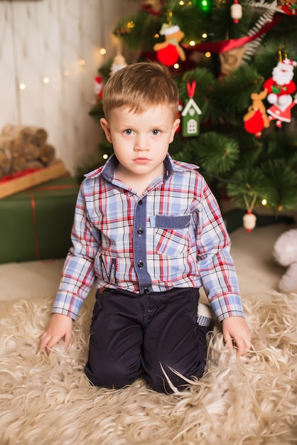 Kleiner Junge, der vor Weihnachtsbaum sitzt