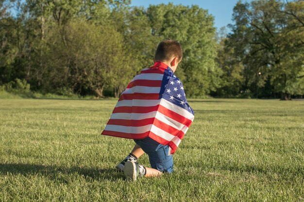 Kleiner Junge feiert den Unabhängigkeitstag der USA am 4. Juli. Kind läuft mit der amerikanischen Flagge, dem Symbol der Vereinigten Staaten, über ein Weizenfeld