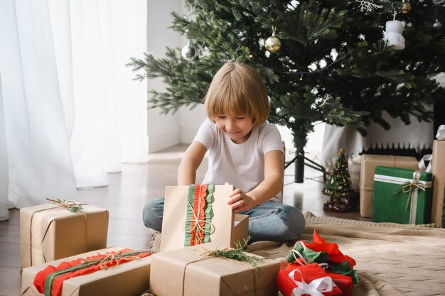 Foto kleiner junge feiert weihnachten zu hause und packt geschenke aus