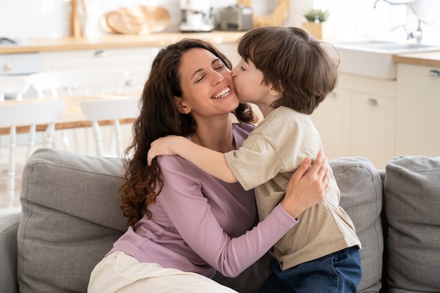 Kleiner Junge gibt Mama einen zärtlichen Kuss in die Wange, der die alleinerziehende Mutter am Muttertag umarmt oder zum Geburtstag grüßt. Süßer Sohn von 5, der liebevolle Mama umarmt, zeigt Liebe und Fürsorge. Elternschaft und glückliches Familienkonzept