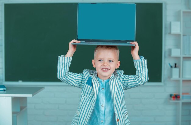 Kleiner Junge hält Laptop auf dem Kopf und lernt Lektion in der Schule mit Gadget