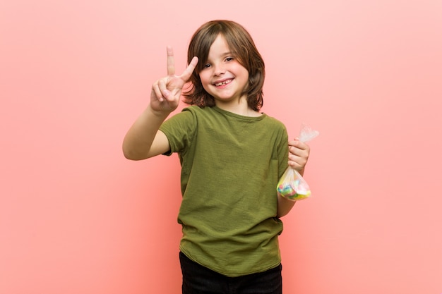Kleiner Junge hält Süßigkeiten, die Nummer zwei mit den Fingern zeigen