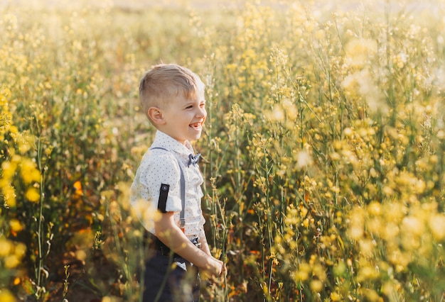 Kleiner Junge hat Spaß und winkt im Sommer in der Natur mit den Händen zur Kamera. Süßes entzückendes Kind in einem Rapsfeld, Nahaufnahme Porträt