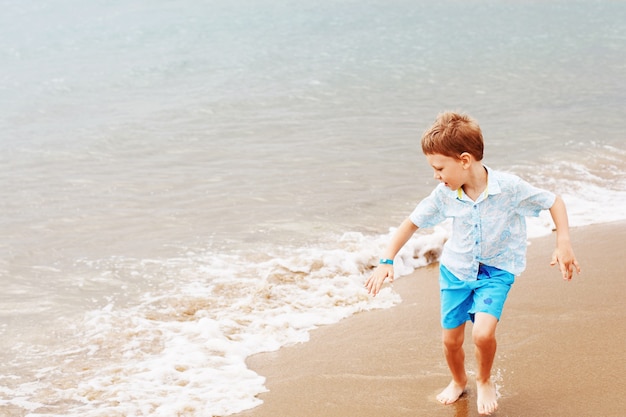 Kleiner Junge im Hemd und in den Shorts auf dem Strandsand.