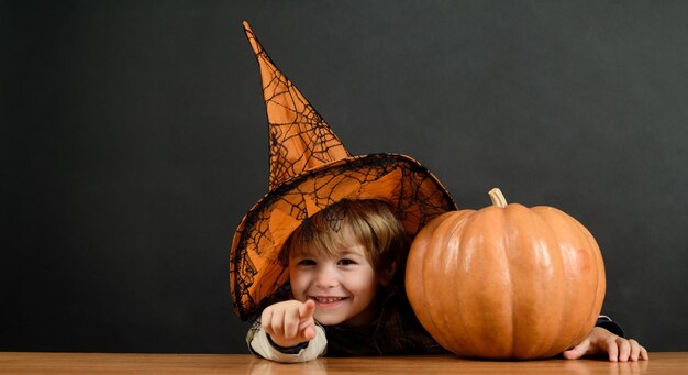 Kleiner Junge im Hexenhut mit Halloween-Kürbis, der auf Sie zeigt, Süßes sonst gibt's Saures Vorbereitung Halloween