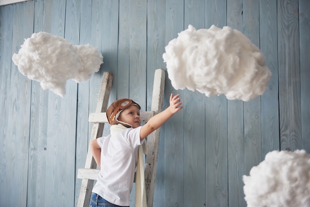 Kleiner Junge im Versuchshut, der auf der Leiter in steht. Erreiche den Himmel. Berühre die Wolken