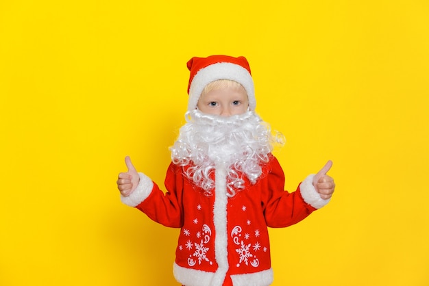 Kleiner Junge im Weihnachtsmann-Kostüm mit weißem Bart zeigt Daumen hoch Geste mit den Händen