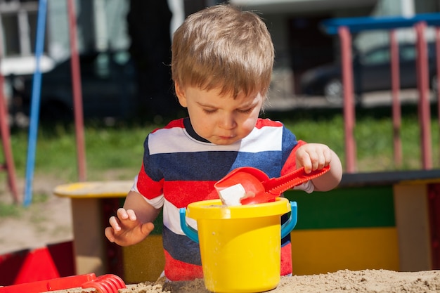 Kleiner Junge in einem bunten T-Shirt spielt im Sandkasten