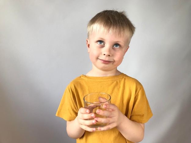 kleiner Junge in einem gelben T-Shirt trinkt Wasser