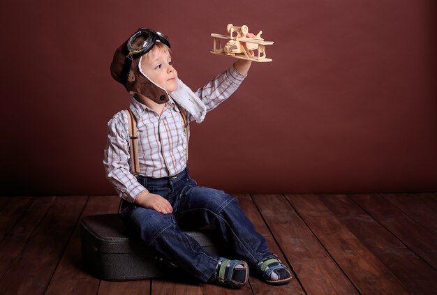 Kleiner Junge in einem Helm spielt mit einem Holzflugzeug. Der Junge träumt davon, Pilot zu werden. Urlaub der Männer