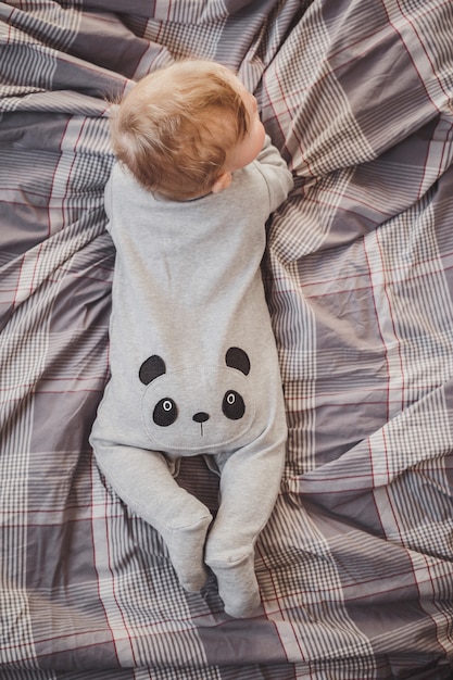 Kleiner Junge in einem Pandakostüm liegt auf dem Bett.