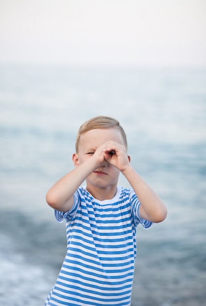 Kleiner Junge in gestreiftem T-Shirt, das auf dem Strand mit undeutlichem Hintergrund durch das Meer spielt