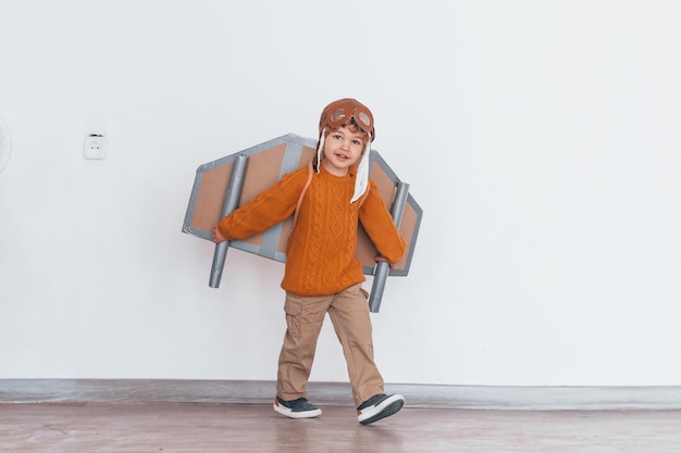 Kleiner Junge in Retro-Pilotenuniform, der drinnen mit Spielzeugflugzeug läuft