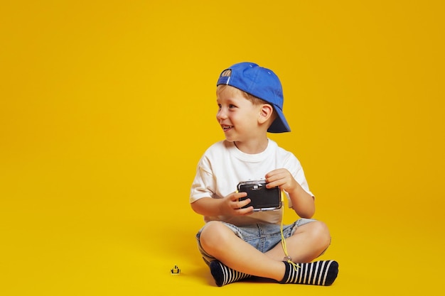 Foto kleiner junge in weißem hemd und blauer mütze hält eine kamera und schaut frei weg