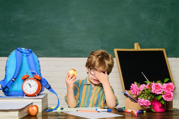 Kleiner Junge isst Apfel in der Mittagspause kleiner Junge hat Mittagessen in der Schule im Klassenzimmer leckeres Essen Mittagessen in der Schule