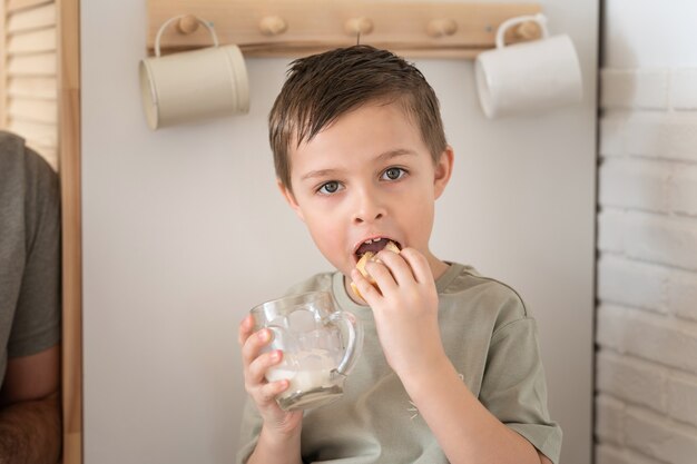 Kleiner Junge isst Brot oder Sandwich und trinkt Milch in der Küche Morgenroutine Konzept