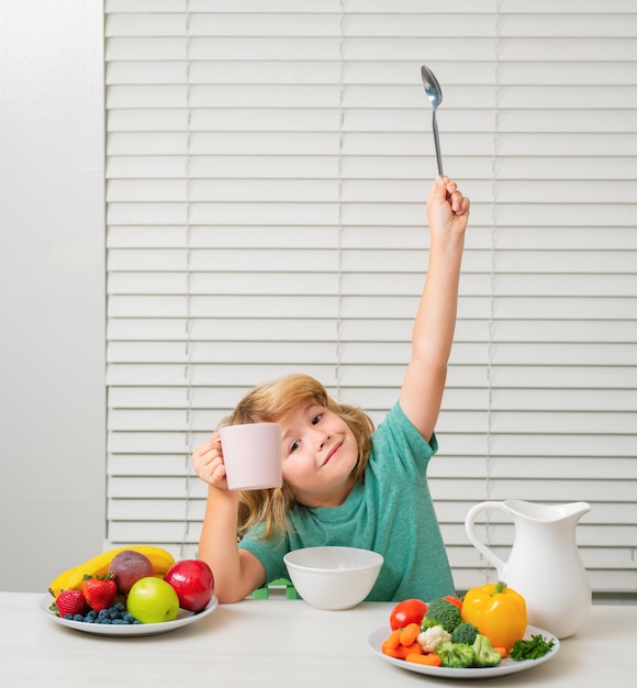 Foto kleiner junge isst gesundes lebensmittel-gemüse-frühstück mit milch, obst und gemüse. kind isst währenddessen