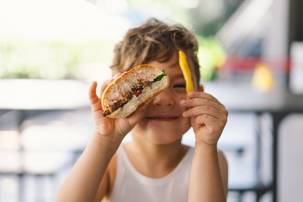 Foto kleiner junge isst sandwich und pommes an einem tisch