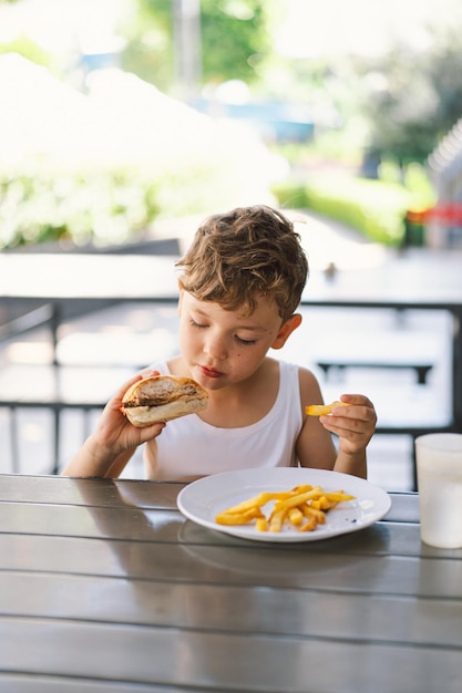 Kleiner Junge isst Sandwich und Pommes an einem Tisch