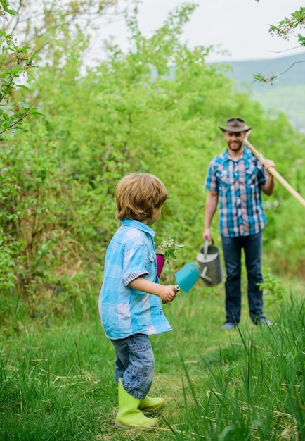 Kleiner Junge Kind helfen Vater in der Landwirtschaft Happy Earth Day Stammbaum Nursing Gießkanne Topf und Hacke Gartengeräte Öko-Bauernhof Vater und Sohn in Cowboy-Hut und Gummistiefeln auf der Ranch