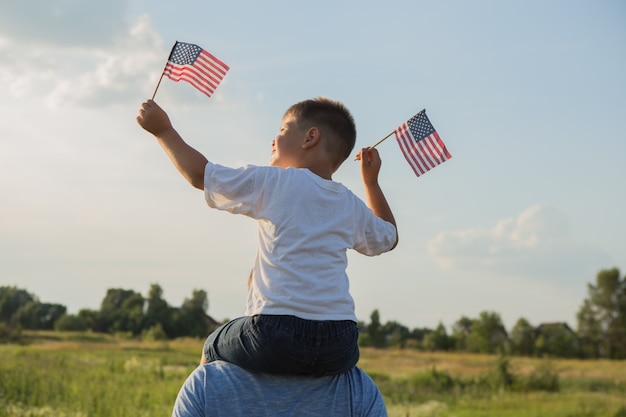 Kleiner Junge lässt die amerikanische Flagge in seinen Händen auf dem Wind auf der grünen Wiese fliegen