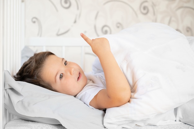 Kleiner Junge lernt zählen. Porträt des verspielten kleinen Jungen im Bett. Konzept des täglichen Regimes.