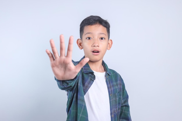 Kleiner Junge macht eine Ablehnungs-Expression, zeigt eine Halt- oder Keine-Handgest auf grauem Hintergrund