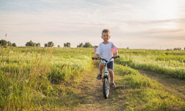 Kleiner Junge mit amerikanischer Flagge auf seinem Fahrrad auf der grünen Wiese