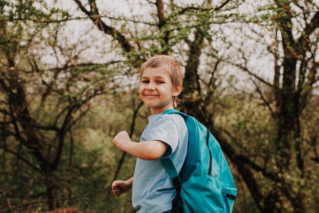 Kleiner Junge mit blauem Rucksack auf dem Rückweg von der Schule Schuljunge, der sich nach dem Unterricht glücklich fühlt und nicht in der Schule ist Outdor-Seitenporträt auf frühem Frühlingsparkhintergrund