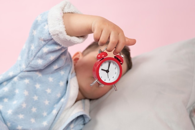 Kleiner Junge mit einem roten Wecker in seinen Händen Morgenkonzept Children39s schlafen Hochwertiges Foto