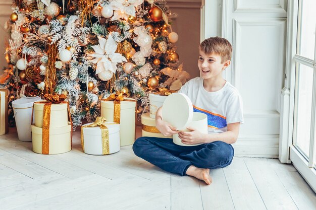 Kleiner Junge mit Geschenkbox nahe Weihnachtsbaum zu Hause