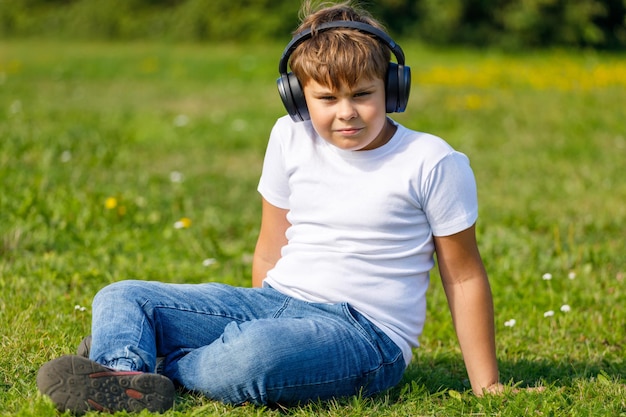 kleiner Junge mit Kopfhörern, der Musik hört, während er auf dem Gras im Park sitzt