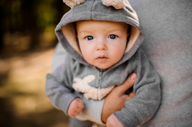 Kleiner Junge mit nachdenklichen grauen Augen sieht aufmerksam aus, wie er an den Händen des Vaters sitzt