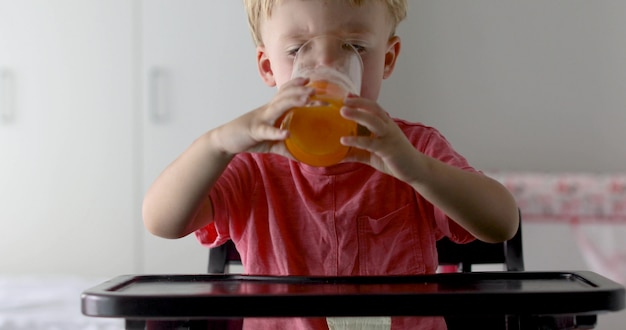 Kleiner Junge mit Orangen und Saft. Glücklicher kleiner Junge, der zu Hause Orangensaft trinkt