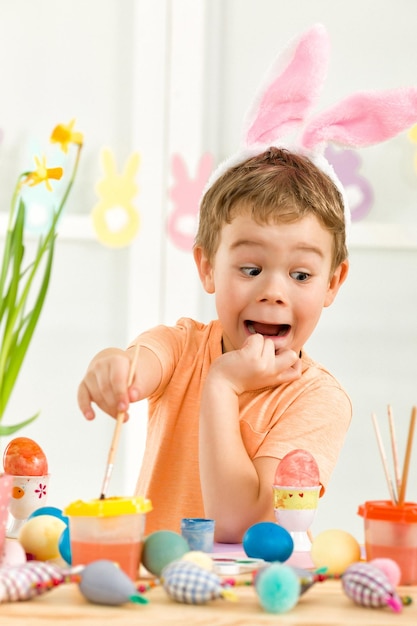 Kleiner Junge mit Osterhasenohren, der Ostereier malt