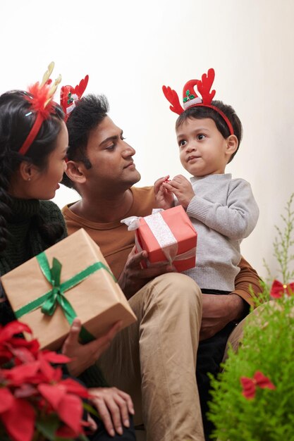 Kleiner Junge mit Rentiergeweih-Stirnband erhält Weihnachtsgeschenke von seiner Mutter und seinem Vater