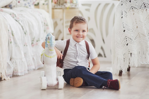 Kleiner Junge mit Rucksack sitzt im Kinderzimmer und spielt Spielzeug. Zum ersten Mal in der Schule. Glückliche Kindheit