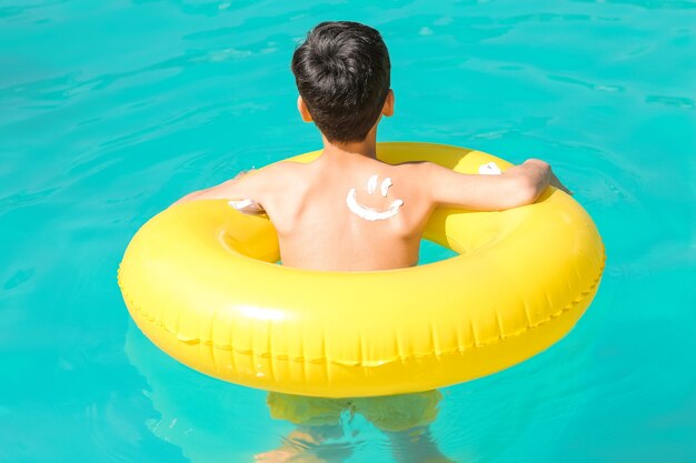 Kleiner Junge mit Sonnenschutzcreme auf seinem Körper und aufblasbarem Ring im Schwimmbad